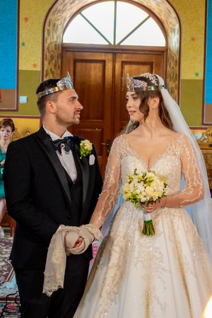 Elegant church wedding with couple in formal attire standing beneath arched windows and wooden doors.