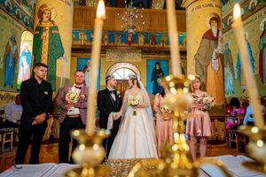 Orthodox church wedding scene with lit candles in foreground and decorated columns and frescoes in background.
