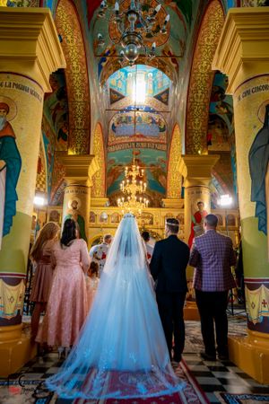 Traditional wedding taking place in a Byzantine-style church with painted murals and golden chandeliers.