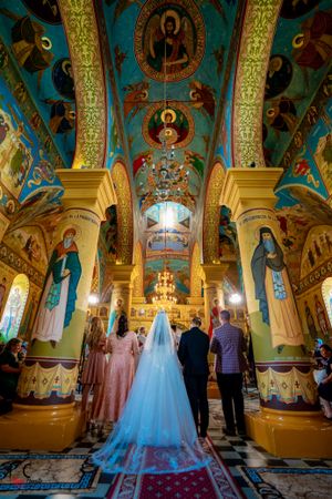 Wedding ceremony in a beautifully decorated Orthodox church with colorful frescoes and ornate columns.