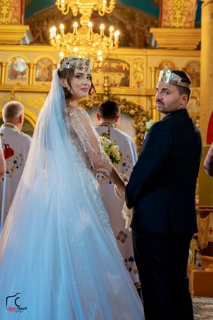 Elegant wedding ceremony in a richly decorated Orthodox church with crystal chandeliers and gilded details.