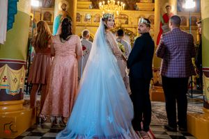 Wedding ceremony in progress inside an ornate Orthodox church with beautiful religious artwork.