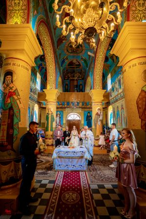 Orthodox wedding ceremony taking place in an ornate church with golden columns and religious murals.