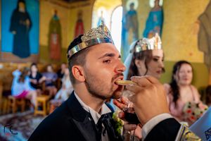 Participant in ceremonial crown drinking wine during Orthodox wedding ritual.