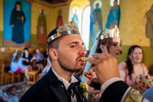 Wedding participant wearing ornate crown sips from ceremonial wine cup in church.