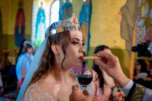 Participant in wedding ceremony wearing crown and formal attire drinking ritual wine.