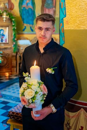 Groomsman holding a white ceremonial candle with floral decorations in an Orthodox church.