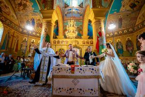 Wide angle shot of Orthodox church interior during wedding ceremony with painted walls and chandeliers.
