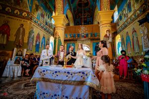 Wedding ceremony taking place in an ornately decorated Orthodox church with colorful frescoes and golden details.