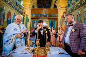 Orthodox wedding ceremony taking place in an ornate church with golden columns and religious murals.