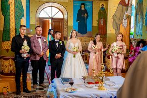 Wedding party gathered in Orthodox church decorated with colorful frescoes and golden ornaments.