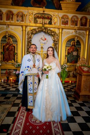Orthodox wedding ceremony with priest in traditional vestments inside gilded church interior.