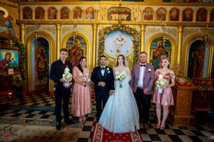 Wedding group photo in an Orthodox church with ornate golden iconostasis and checkered floors.