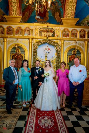 Large wedding group photo in Orthodox church with guests wearing vibrant formal attire.
