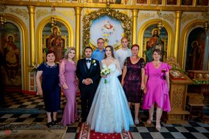 Wedding group photo in front of golden Orthodox church altar with decorative icons.
