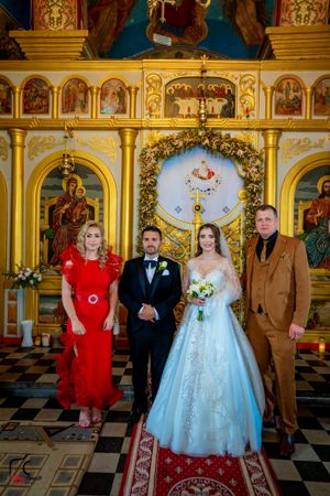 Wedding party stands on red carpet in front of ornate golden Orthodox church altar.