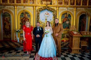 Wedding celebration in Orthodox church interior with golden iconostasis and decorative religious artwork.