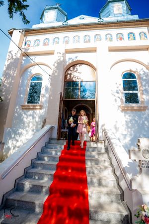 Sunlit white Orthodox church facade with red carpet stairway entrance.