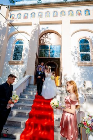 Wedding ceremony exit on red-carpeted steps of white Orthodox church building.