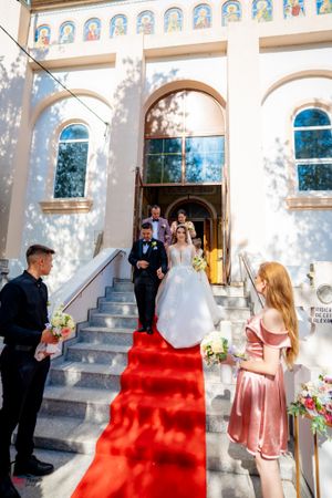Wedding ceremony exit with red carpet and white doves against classical church architecture.