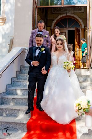 Couple descends church steps on vibrant red carpet during wedding celebration.