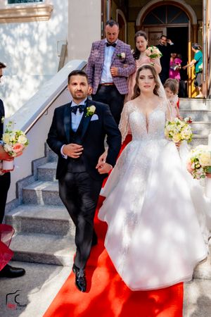 Wedding party walks down stone steps covered with bright red carpet outside historic church.