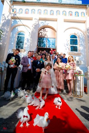 Wedding celebration with guests and white doves on red carpet at church entrance.
