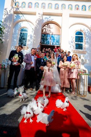 Wedding party and guests watch white doves on red carpet outside church.