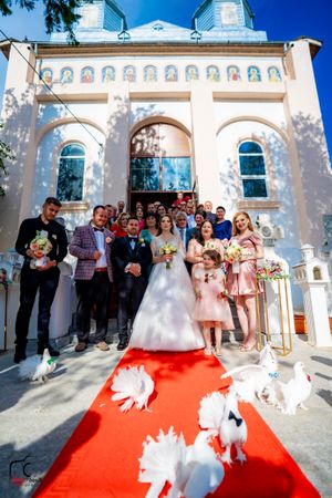 Panoramic view of wedding celebration with guests and doves outside church entrance.