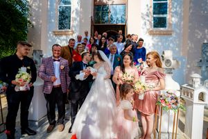 Wedding party members stand in a line against white church walls with arched windows.