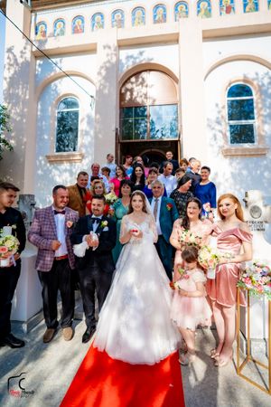 Wedding group photo session with white church architecture and decorative arches in background.