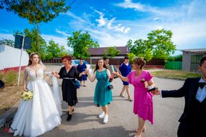 Wedding party members dance in a line outdoors under bright blue summer sky.
