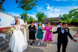 Wedding guests form a dancing line in a sunny outdoor parking area.