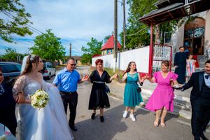 Wedding party members dance in a line wearing vibrant dresses outside a historic building.