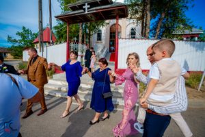 Wedding party members dance energetically in casual attire outside on a bright summer day.