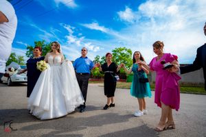 A wedding party dances together outside under bright blue skies during summer celebrations.
