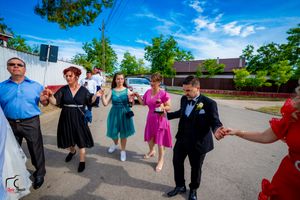 Wedding celebration line dance continues outdoors with bright blue sky and trees in background.