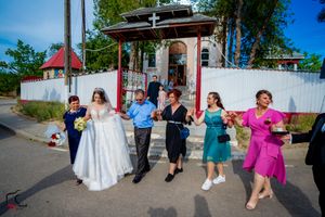 Wedding party dances in a line outside on a sunny day with colorful dresses and suits.