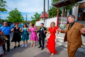 Wedding group dances in formation wearing vibrant formal attire under blue skies.