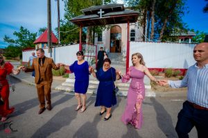 Wedding party members dance in coordinated movements on a sunny street.