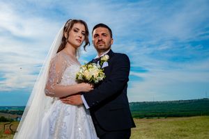 Romantic wedding portrait of couple in formal attire against blue sky and rolling landscape.