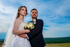 Intimate wedding portrait captured against serene countryside landscape and blue skies.