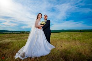 Romantic wedding photo in rustic field setting with dramatic blue sky backdrop.