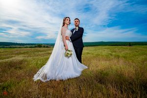 Wedding couple poses in scenic meadow with expansive blue sky and rolling hills.