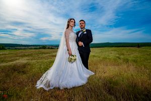 Elegant wedding portrait in natural meadow setting with dramatic cloud-filled sky.