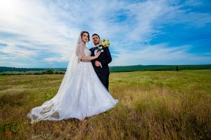 Wedding couple poses in a scenic meadow under bright blue skies with rolling hills in the background.