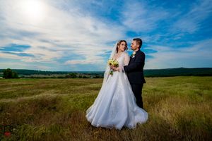 Wedding couple embraces in a sun-drenched field with panoramic countryside views.