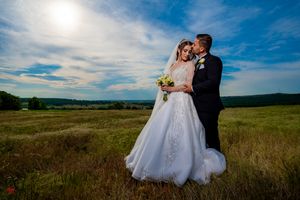 Elegant bridal couple poses in sunlit meadow with expansive landscape views.