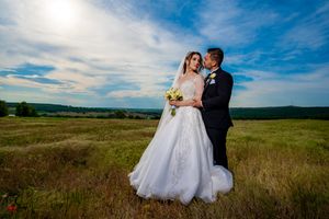 Newlyweds share an intimate moment in a golden field under bright blue summer skies.