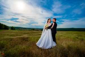 Wedding photography in a rustic field setting with dramatic clouds and natural lighting.